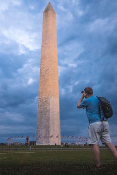 a man standing in front of the washington monument talking on his cell phone while holding a backpack