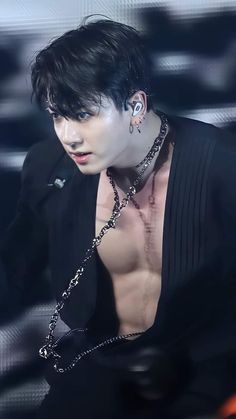 a man with black hair and piercings on his chest wearing a chain around his neck