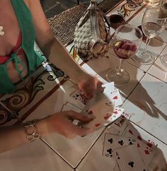 a woman in a green top is playing cards with wine glasses and other items on the table