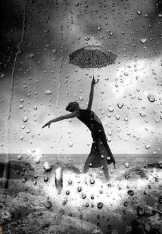 a black and white photo of a woman holding an umbrella over her head in the rain