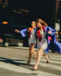 two girls in graduation gowns running across the street