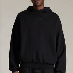 The Fear Of God Essentials Jet Black Hoodie Features An Oversized Fit, A Mock Neckline, Long Sleeves, Side Seam Pockets, An Attached Hood, Contrast Stretch Binding, And Rubber Brand Labels At The Center Front And Upper Back. Solid Color Hoodie Attached Hood Long Sleeves Mock Neckline Dropped Shoulders Side Hand Pockets Front & Back Rubber Brand Labels Contrast Stretch Binding Relaxed Fit 80% Cotton, 20% Polyester Brushed Back Fleece Hand Wash, Flat Or Line Dry Oversized Funnel Neck Hoodie With Drawstring, Oversized Funnel Neck Hoodie For Streetwear, Oversized Black Top With Adjustable Hood, Urban Hoodie With Funnel Neck For Streetwear, Black Hoodie With Drawstring For Loungewear, Urban Funnel Neck Hoodie For Streetwear, Oversized Hoodie With Ribbed Cuffs And Funnel Neck, Oversized Sweatshirt With Drawstring Hood And Funnel Neck, Oversized Funnel Neck Sweatshirt With Drawstring Hood