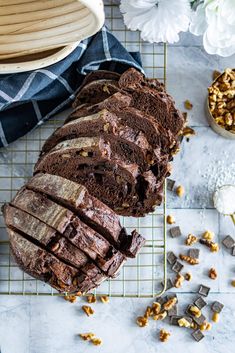 a loaf of chocolate cake sitting on top of a cooling rack next to some nuts