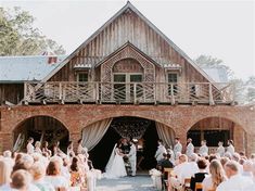 a couple getting married in front of an old barn with their wedding party on the other side