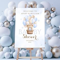 a welcome sign for a baby shower with balloons and a teddy bear in a basket