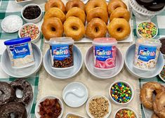 an assortment of doughnuts and other treats are on the table with bowls of cereal