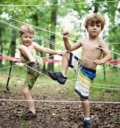 two young boys playing in the woods with tennis racquets and ball net