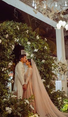 a bride and groom standing next to each other in front of a flower covered wall