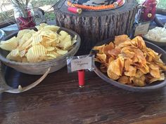 two bowls filled with chips on top of a wooden table next to a tree stump