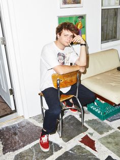 a young man sitting in a chair with his hand on his head and looking at the camera