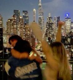 two people standing in front of a cityscape at night with their arms up