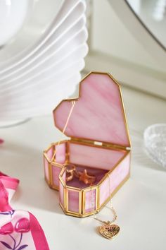 an open pink and gold jewelry box sitting on top of a table next to plates