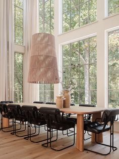 a dining room table with chairs and a vase on it in front of large windows