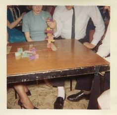 two people sitting at a table playing with blocks and a teddy bear in front of them