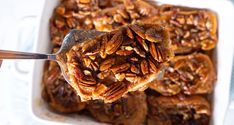 a spoonful of pecans is being lifted from a casserole dish