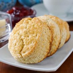 three biscuits on a white plate with butter and jelly in the backgroung