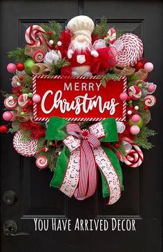 a christmas wreath with candy canes on the front door and merry christmas sign above it