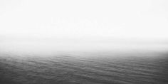 black and white photograph of the ocean on a foggy day with no one in it