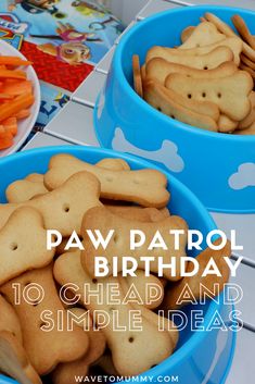 two blue bowls filled with dog shaped cookies next to carrots and pretzels