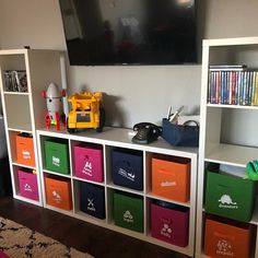 there is a television mounted on the wall above some bookshelves with colorful bins