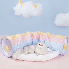 a white cat is laying in a pink, blue and yellow pet bed with stars on it