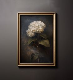 a white flower in a gold frame hanging on a gray wall next to a black wall