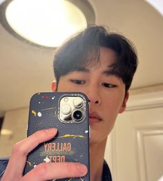 a young man taking a selfie with his cell phone in front of the mirror