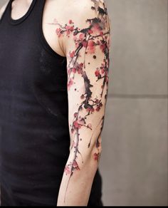 a man wearing a black tank top with red flowers on his arm and shoulder tattoo