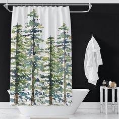 a white bath tub sitting next to a shower curtain with trees on it in front of a black wall