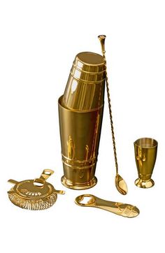 a gold colored cocktail set with two cups, spoons and tongs on a white background