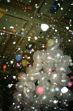 white balloons are floating in the air with confetti all around them on a ceiling