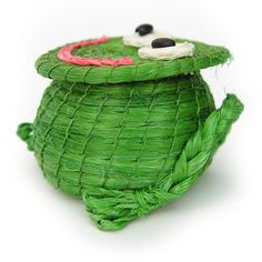 a small green pot with eyes on it's lid and some grass in the shape of a frog