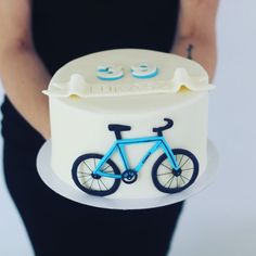 a woman holding a cake with a bicycle on it and the number 33 on top