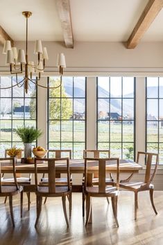 a dining room table and chairs with large windows in the back ground, overlooking an open field