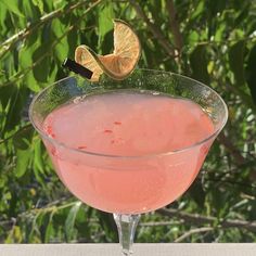 a pink drink in a glass with an orange slice sticking out of the rim and garnish