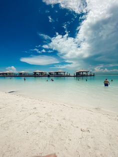 people are swimming in the clear blue water on a beach with overhangs and thatched huts