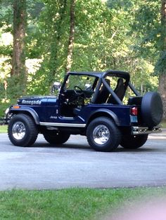 a blue jeep is parked on the side of the road in front of some trees