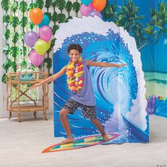 a young boy on a surfboard in front of a photo booth with balloons and streamers