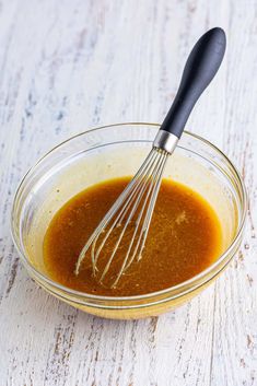 a whisk in a glass bowl filled with sauce on top of a wooden table