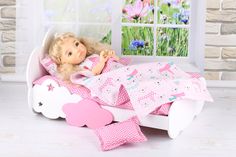 a doll is laying in a bed with pink sheets and pillows on the floor next to a window