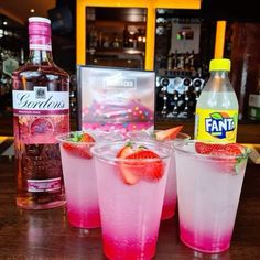 three glasses filled with pink liquid and strawberries next to a bottle of booze