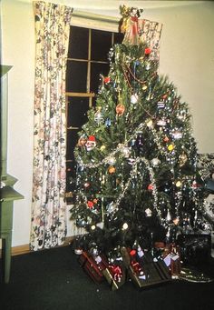 a decorated christmas tree sitting in front of a window with presents under it on the floor