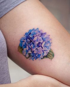 a woman's thigh with a blue and purple flower tattoo on the side of her leg