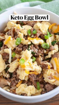 a white bowl filled with eggs and meat on top of a wooden table next to a green towel