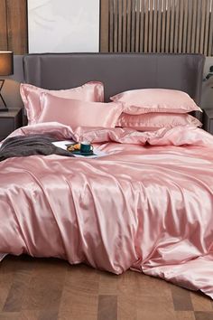 a bed with pink sheets and pillows on top of it in a room that has wood flooring