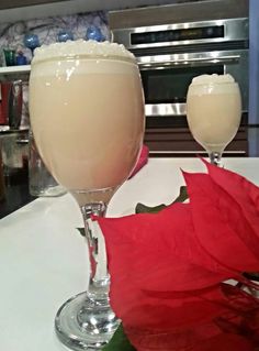 two glasses filled with liquid sitting on top of a counter next to a red flower