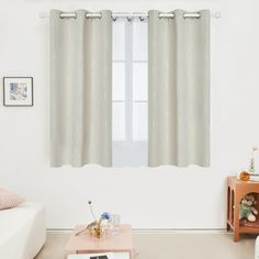 a living room with white walls and curtains on the windowsills, a coffee table in front of a couch