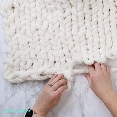 someone is crocheting a blanket on top of a marble surface with their hands