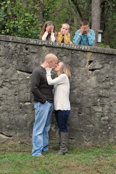 a man and woman kissing in front of a stone wall with people looking at them