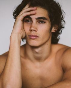 a shirtless young man holding his hand to his head while looking at the camera